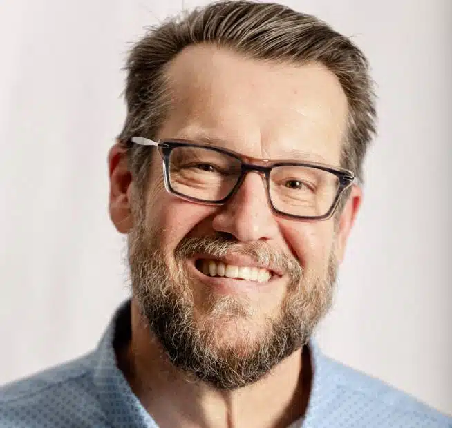 a man wearing glasses and smiling at the camera